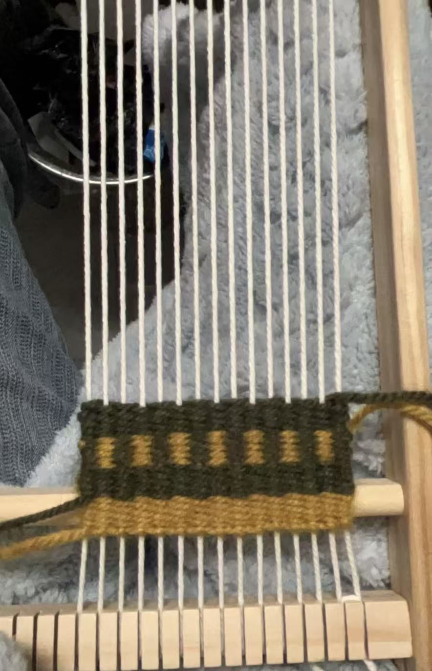 Customer weaving a green and gold coaster on a wooden loom