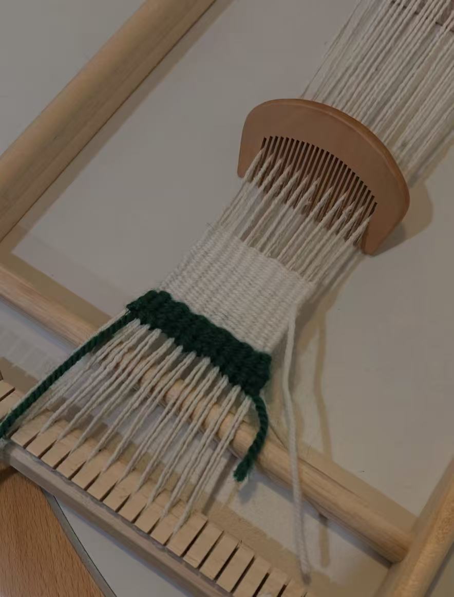 Beginner weaving cream and green yarn on a wooden loom