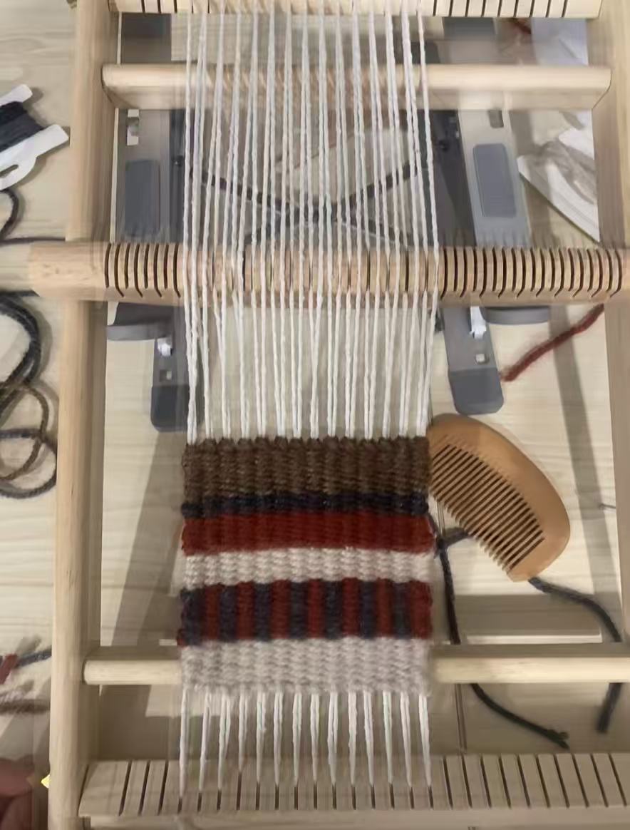 Striped coaster in warm yarn colors on a wooden loom