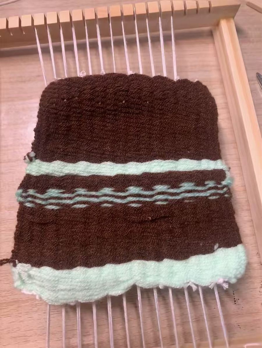 Beginner woven brown and mint piece on a wooden loom